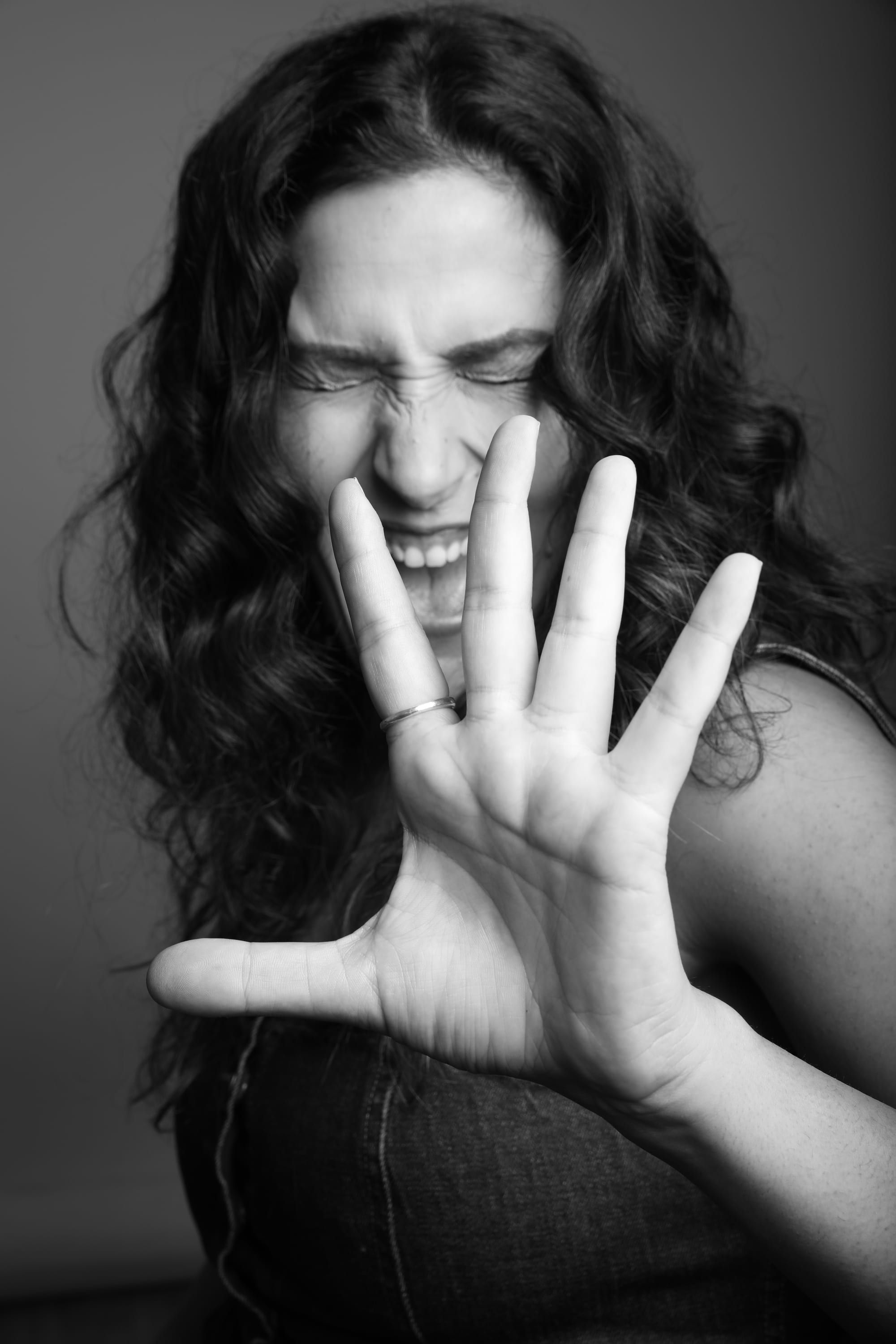 Noam Shuster-Eliassi laughing with her eyes shut, palm raised towards the camera